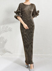 A woman models a floor-length pleated maxi dress with ruffled elbow-length sleeves. The dress has a metallic, shimmering dark brown and bronze color.